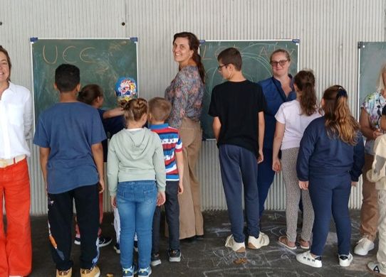 Les élèves de l'UEE debouts de dos, face aux tableaux et avec leurs professeurs